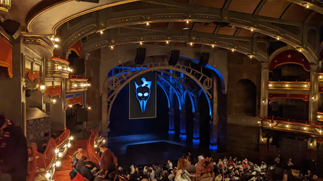 Interior of a theater with ornate ceiling, stage lighting, and audience seating visible.