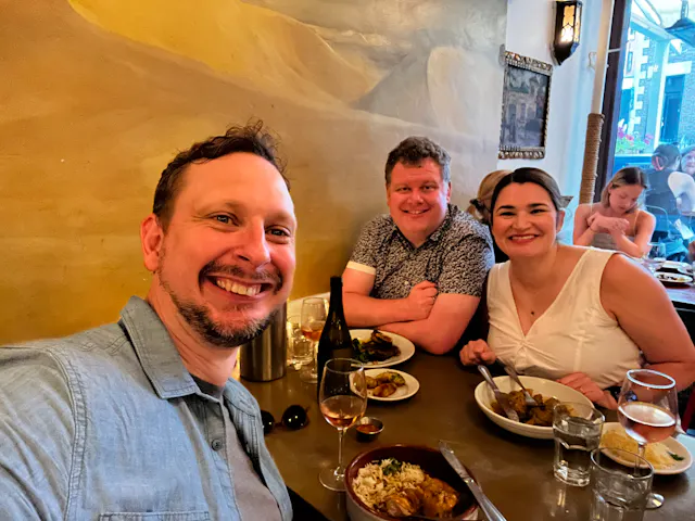Three people smiling at a restaurant table with food and wine glasses.