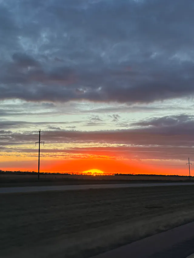 Vivid orange and red sunset over a flat highway landscape with utility poles.