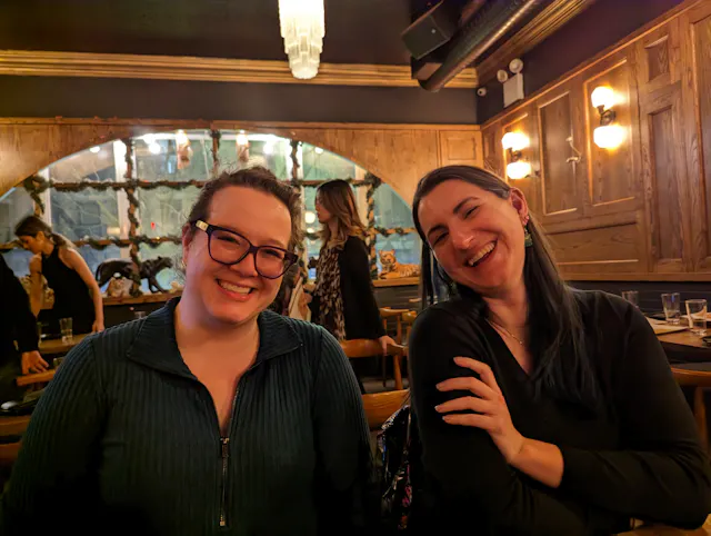 Two women smiling together at a dimly lit restaurant booth.