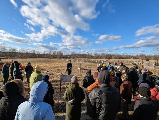 A crowd of people gathered outdoors at a wintry open field event under blue skies.