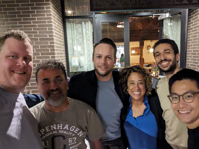 Six people taking a group selfie together indoors at a restaurant.