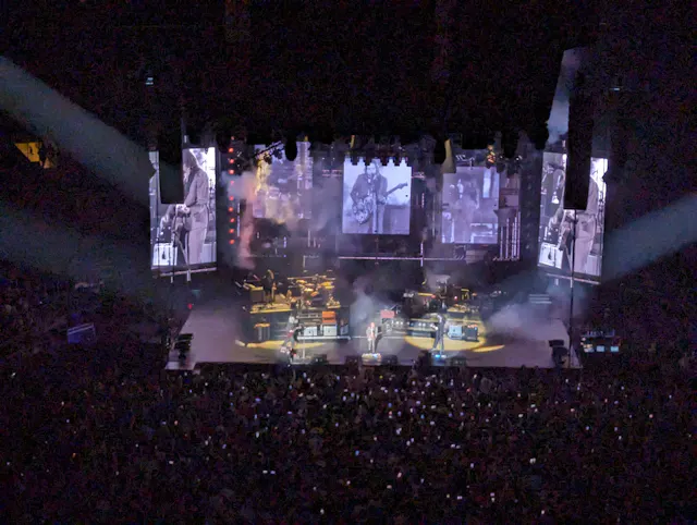 Aerial view of a packed concert arena with colorful stage lighting and large video screens.