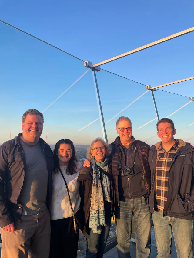 Five people posing together on an outdoor observation deck at sunset with a city skyline behind them.