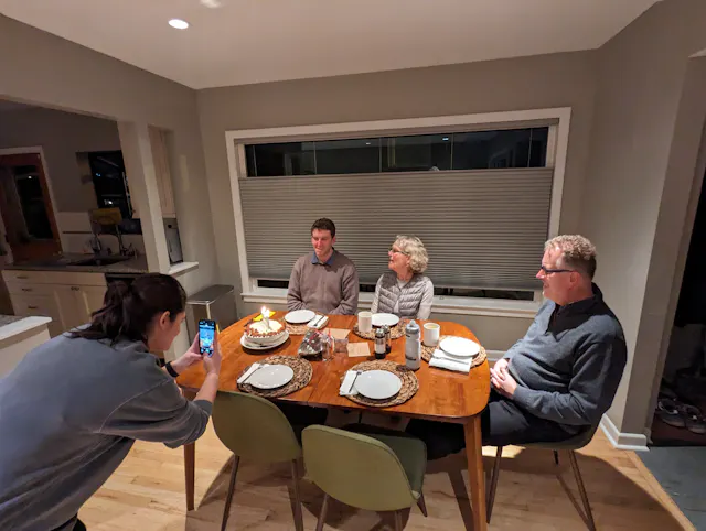 Four people seated around a dinner table in a warmly lit home dining room.