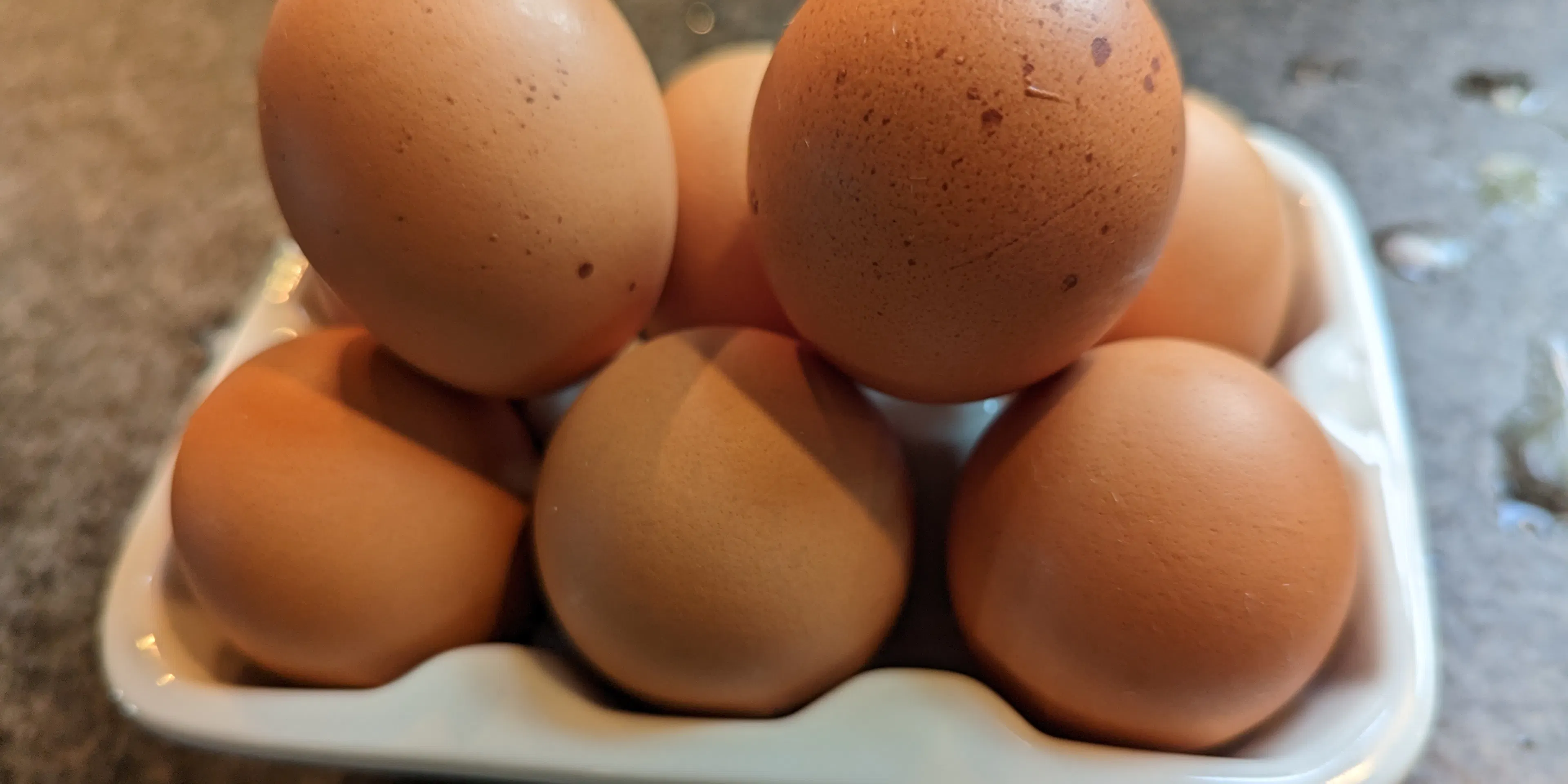Several brown eggs are piled in a white ceramic egg holder on a countertop.