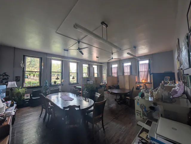 Interior of a blue-walled studio space with ceiling fan, round dining table, and various furnishings and plants.