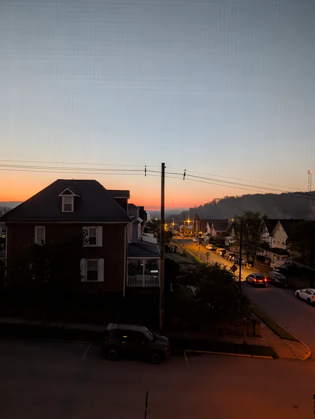 Sunrise over a small Pennsylvania town seen from a window, with a tall red brick house in the foreground and an orange band of light on the horizon