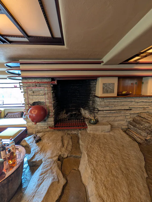 Interior of Fallingwater showing the great hearth built into natural bedrock, with a red kettle hanging on a swing arm beside the fireplace