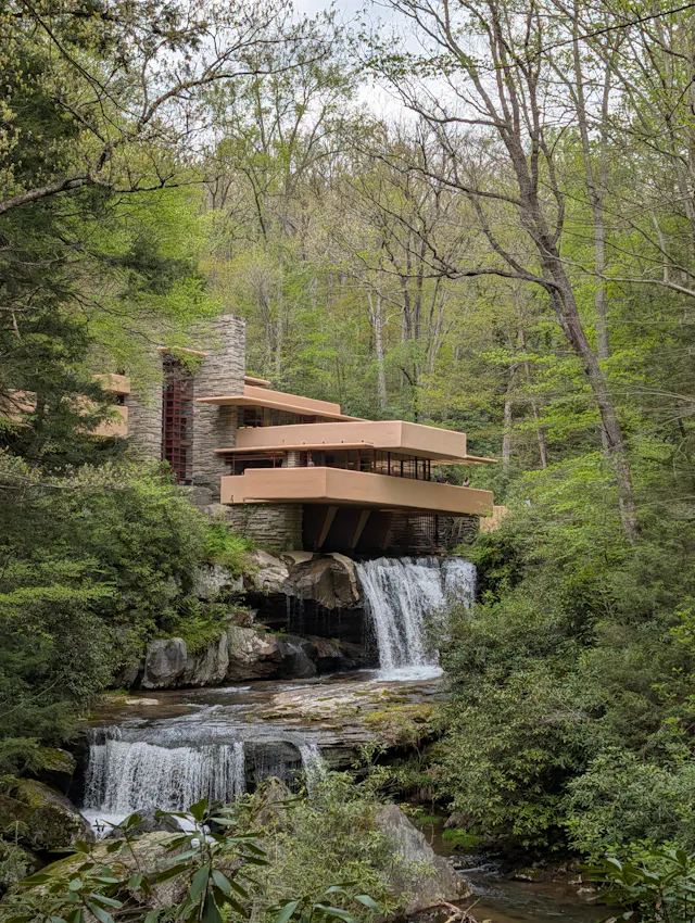 Fallingwater seen from downstream, with its tan cantilevered terraces extending out over the waterfall and surrounded by trees